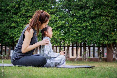 Family Asian Mother teacher training yoga child daughter on a yoga mat at home garden. Family outdoors. Parent with child spends time together. exercise at home concept and new normal.