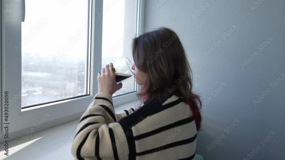 Side view of a nostalgic young woman drinking a coffee while looking through the window at home or during break at the office Side view of a nostalgic young woman drinking a coffee while looking through the window at home or during break at the office