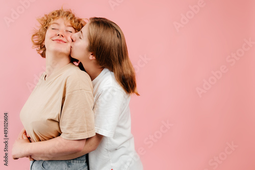 Two young generation z LGBT girls in love hugging and kissing, showing their feeling to the wold, posing isolated on pink background. Women and Valentines Day