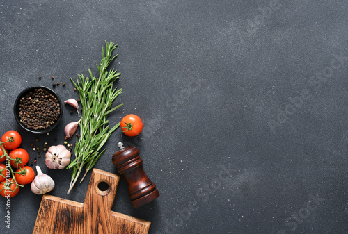 Spices on black concrete background. Wooden board, rosemary and tomatoes on the kitchen table, top view.