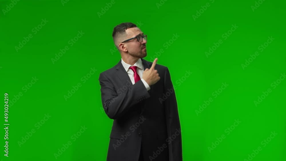 Positive male businessman in a suit smiling and looking at camera points hand to the side, the green studio background. Positive male businessman in a suit smiling and looking at camera points hand to the side, the green studio background.