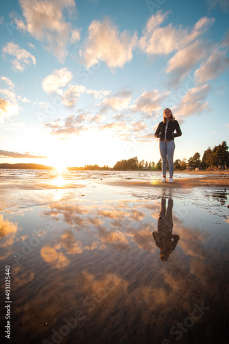 Smiling young brunette athlete walks barefoot on a sandy beach in jeans and a black blouse, enjoying the sunset and the last warm rays. Sotkamo, Finland. Discovering Scandinavia. Real people