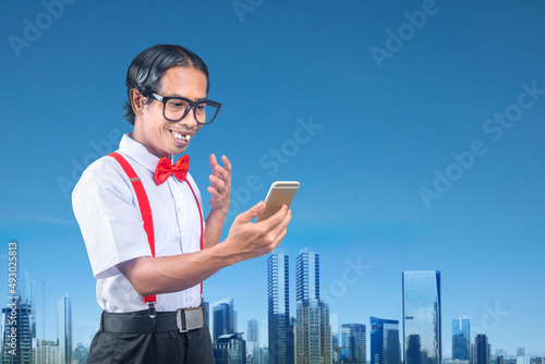 Fototapeta Asian nerd with an ugly face holding mobile phone