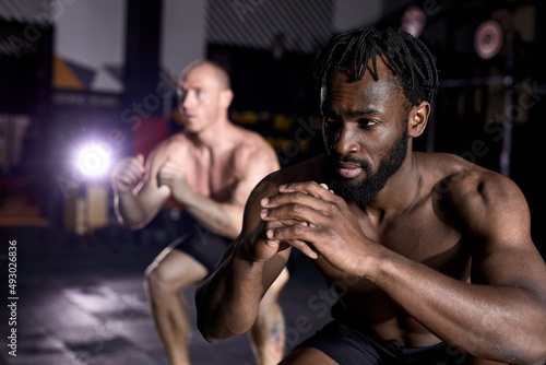 two an athletic men doing box jump exercise. Cross fit, sport and healthy lifestyle concept. African and caucasian shirtless sportsmen engaged in sport, concentrated and motivated. focus on black man