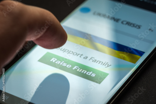 Close-up finger pressing raise funds button on smartphone screen. Donation money online concept