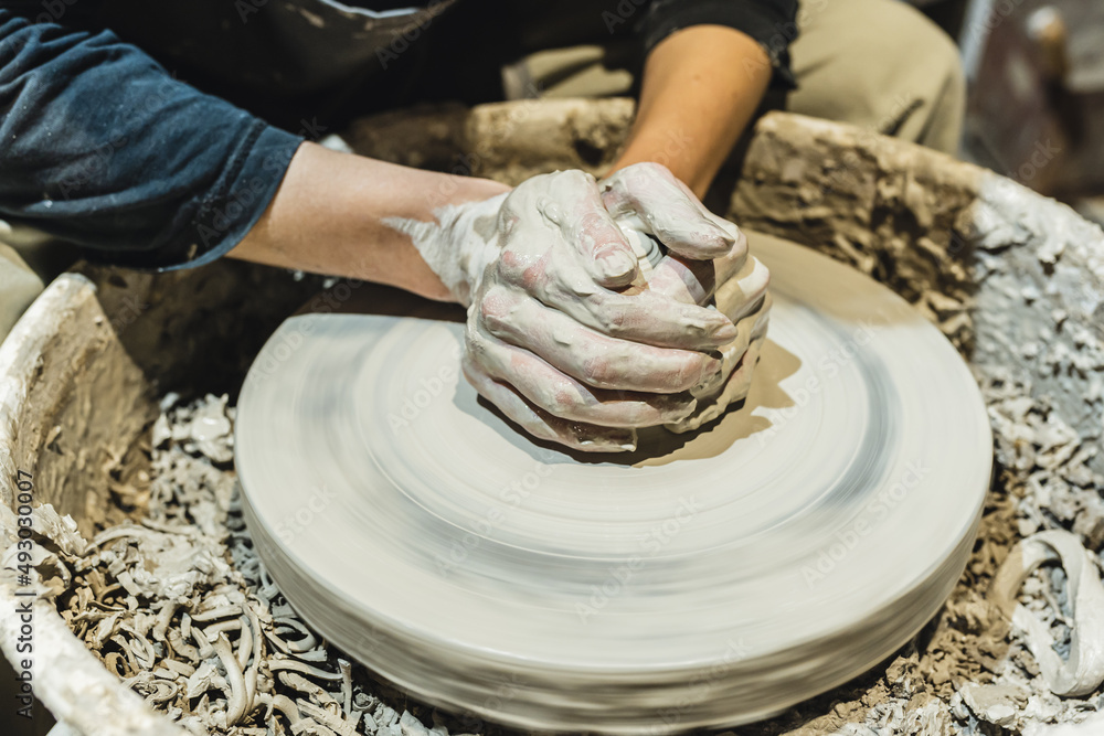 potter's female hands, soiled in clay, form clay lump on potter's wheel. Craft clay pottery, hobby folk art