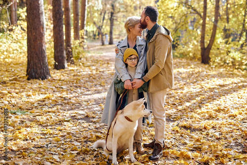 portrait of friendly family with dog posing at camera in autumn park, in love. Attractive lady with husband and son enjoy spending weekends in autumn forest, at sunny day. rest, togetherness