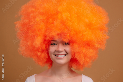 Smiling young orange haired woman on beige background. Close up portrait.