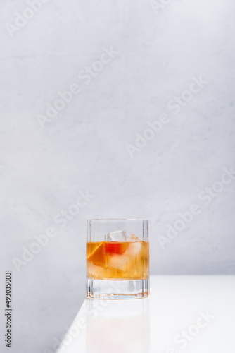 Vaso de vermut rojo con hielo decorado con cerezas y rodajas de naranja sobre mesa blanca	
