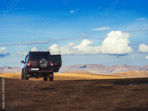 Φωτογραφία A black SUV stands in a golden autumn field located in the highlands under a blue sky with occasional white cumulus clouds