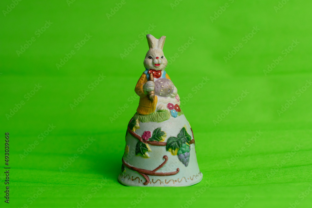 Beautiful handmade ceramic bell with Easter bunny on top painted with spring flowers isolated on green background.