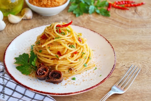 Italian Traditional Dish"Spaghetti con acciughe e pangrattato",spaghetti with anchovy,roasted bread crumbs,garlics,olive oil,chilli peppers and parleys on plate with wooden background.Copy space