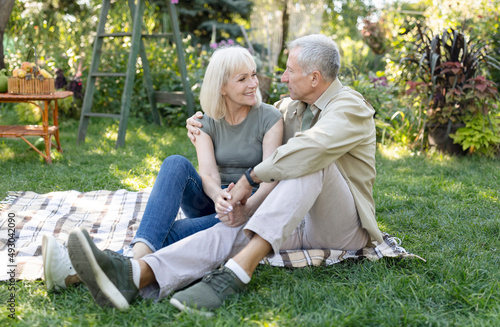Happy loving senior couple having picnic in garden, embracing and smiling to each other, sitting together outdoors