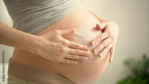 Close up of pregnant woman applying moisturizing cream on her belly. Health care and medicine during pregnancy. Concept of pregnancy, maternity, preparation and expectation
