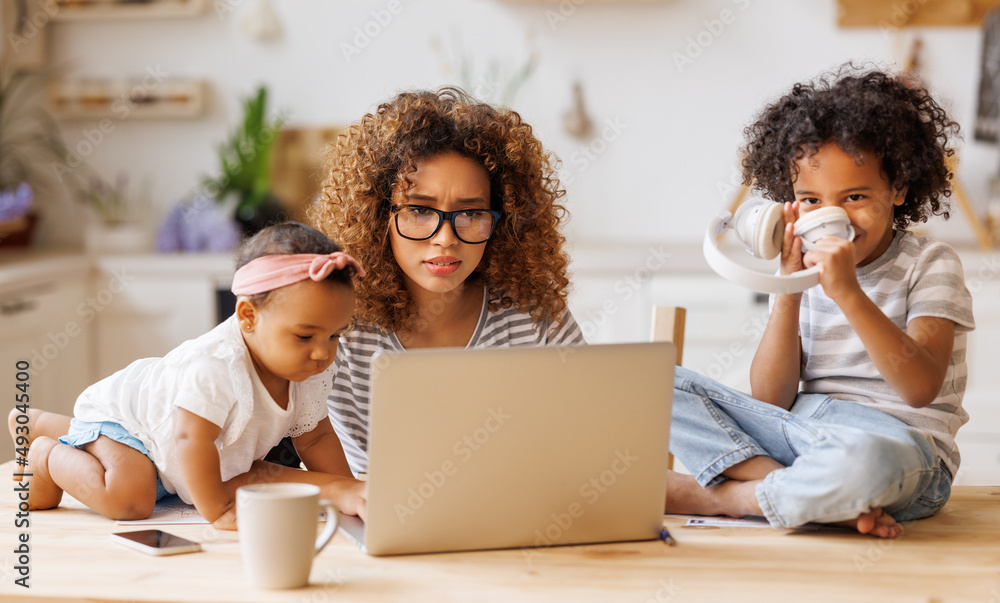 Young irritated African-American mother freelancer trying to work while
