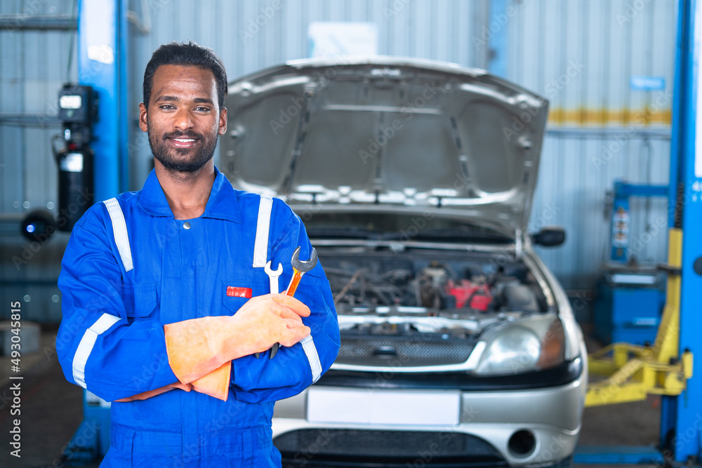 portrait shot of fsmiling Car mechanic wih tool in hand looking at camera while standing with arms crossed - concept confident, repair and maintenance service and garage expertise portrait shot of fsmiling Car mechanic wih tool in hand looking at camera while standing with arms crossed - concept confident, repair and maintenance service and garage expertise