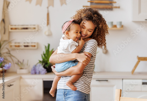 Happy, cheerful ethnic mom holds a laughing baby daughter in her arms