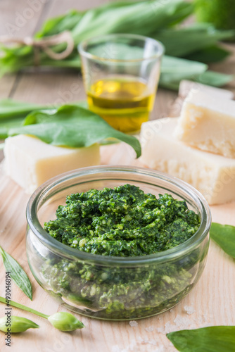 Homemade wild garlic pesto in a glass bowl on wooden background, decorated with some of the ingredients, vertical