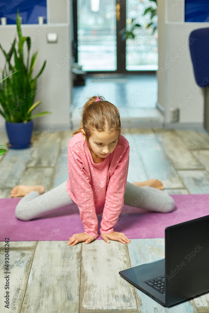 Φωτογραφία Little girl watching online video on laptop and doing stretching, fitness exerci