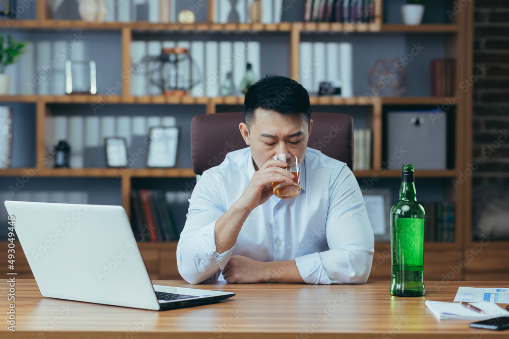 Asian businessman fails, man in despair drinks hard liquor, sitting late at the table in the office, depressed and hopeless Asian businessman fails, man in despair drinks hard liquor, sitting late at the table in the office, depressed and hopeless