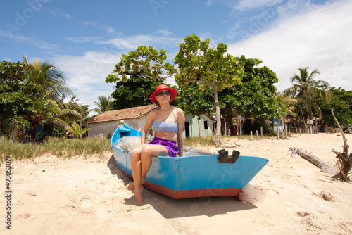 Lady sitting in an old wooden fishing boat enjoying herself at the beach in Corumbau, Bahia, Brazil