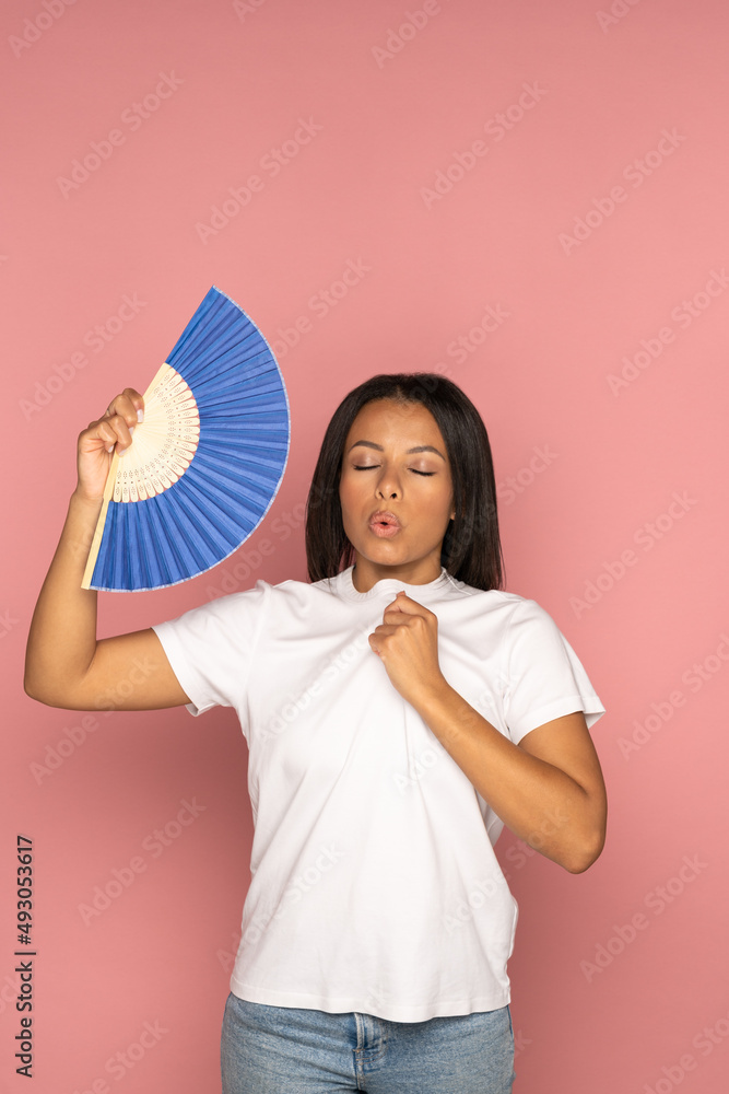 Exhausted african american woman with closed eyes using blue fan suffer from heat sweating, feels sluggish. Black female cooling in hot summer weather, high temperature, isolated on pink background. Exhausted african american woman with closed eyes using blue fan suffer from heat sweating, feels sluggish. Black female cooling in hot summer weather, high temperature, isolated on pink background.