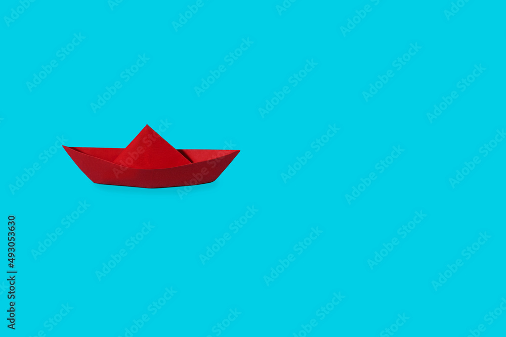 Naklejka premium Red paper boat on a blue background. Overcoming difficulties and leadership concept. Free space for text. Origami ship from red cardboard on a blue background