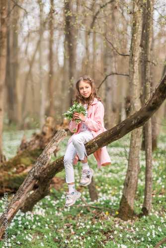 Portrait of a girl with a bouquet of anemone. A child in the spring forest.