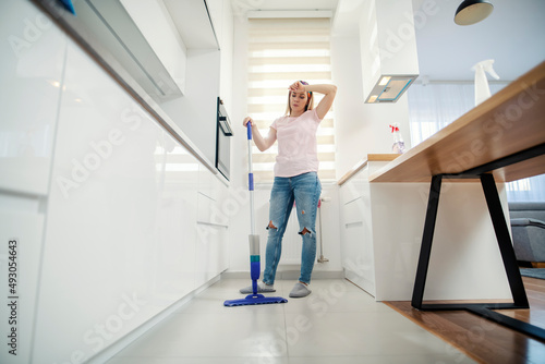 A tired housewife holding mop and taking a break in cleaning floor. © dusanpetkovic1