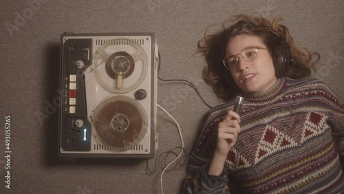 A teenage girl lying on the floor singing her favorite song and recording it in an old fashioned tape recorder