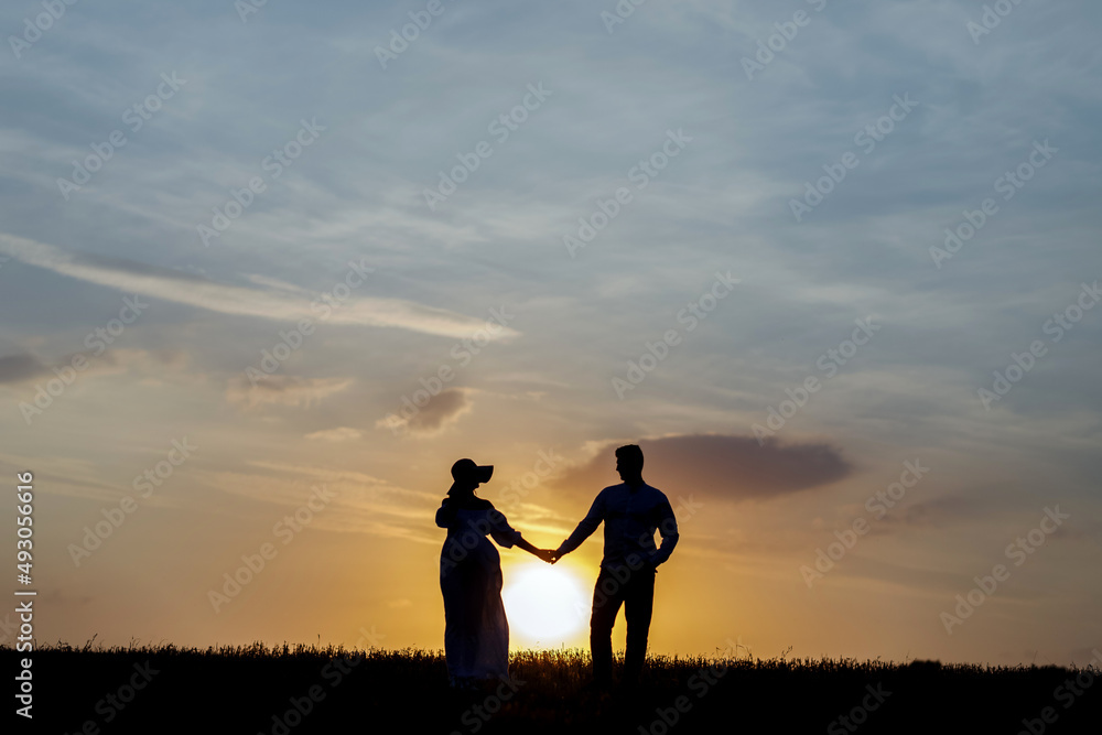 Young couple holding hands on the background of the setting sun on the horizon
