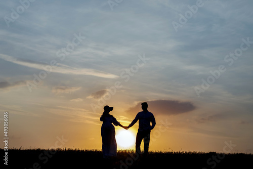 Young couple holding hands on the background of the setting sun on the horizon