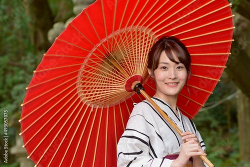 新緑を背景に和傘を手に浴衣を着た微笑む美しい女性のポートレート