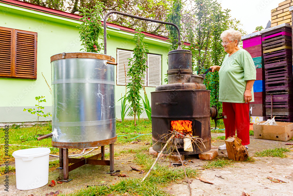 Obraz premium Woman is manually mixing fruit marc in distillation apparatus for making domestic alcohol liquor