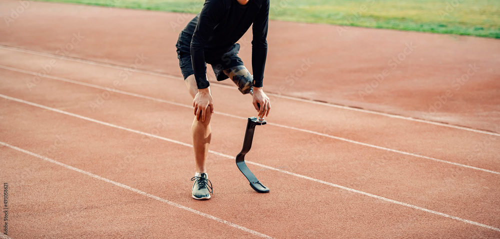 Tired runner with prosthetic leg standing on running track and taking a break.