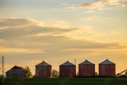 Four small wooden grain bins under a sunset sky in an evening summer landscape