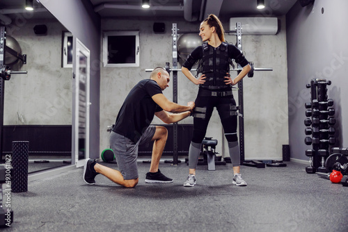 The concept of revolutionary training, coach putting ems suit on a sportswoman in gym.