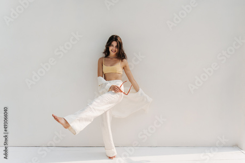 Tela Full length funny young caucasian woman raising leg in front of her while standing against white background