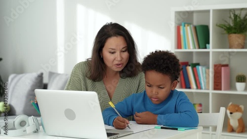 Asian woman and her african son at home, the mother watching her son doing his homework, Social distancing and self isolation in quarantine Covid 19. Mixed race happy family concept. 4k footage
