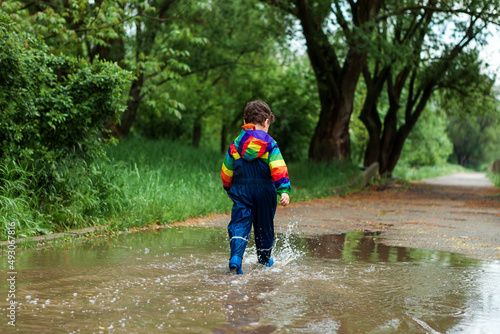 the boy runs and jumps through puddles in a waterproof suit and rubber boots.Bright kurta in the colors of the rainbow