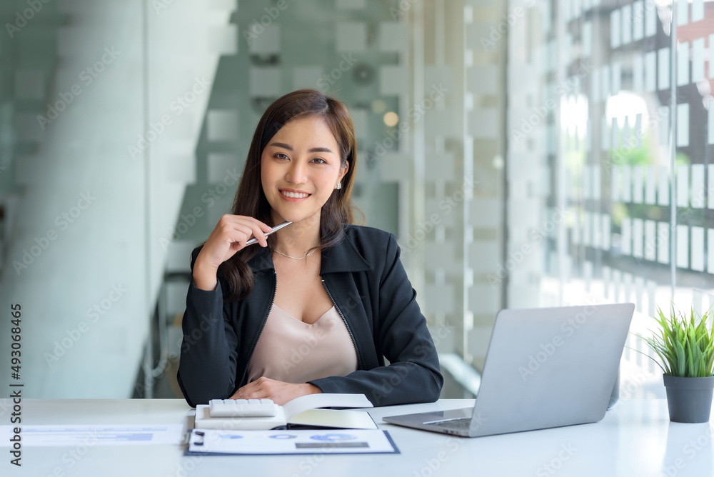 Charming Asian businesswoman working with a laptop at the office. Looking at camera. Charming Asian businesswoman working with a laptop at the office. Looking at camera.