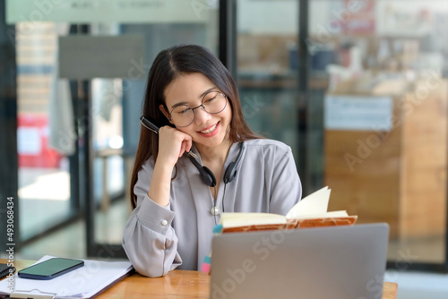 Happy young Asian student woman wearing headphones looking at webcam, looking at camera, during virtual meeting or video call talk.