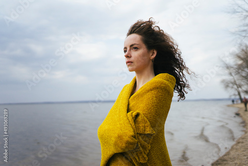 a woman stands on the shore of the lake covered with a yellow cape photo