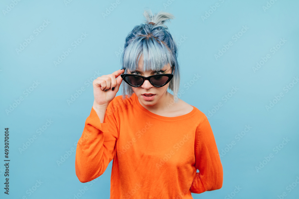 Funny hipster girl with colored hair in sunglasses looks intently at the camera with a serious face. Funny hipster girl with colored hair in sunglasses looks intently at the camera with a serious face.