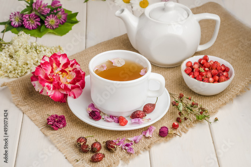 Herbal tea with rosehip and meadowsweet in a white cup on a white wooden table with flowers