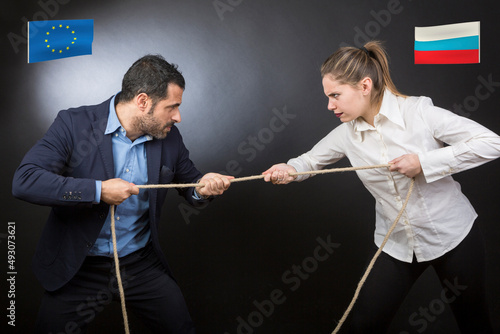 Uomo e donna tirano la corda isolati su sondo nero. Entrambi rappresentano le fazioni opposte tra Russia e Europa photo