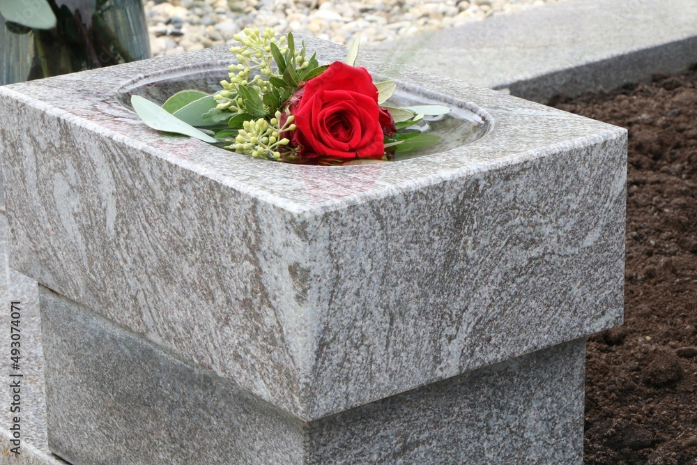 Rote Rose in einem Weihwasserbehälter an einem katholischen Friedhof in Österreich, Grabschmuck, Gedenkstätte, Erinnerung, Trauer, Tod, Bestattung