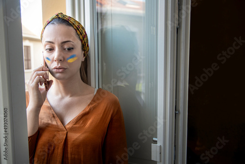 ritratto di una ragazza bionda con i colori dell'Ucraina disegnati sul viso che parla seria al telefono photo