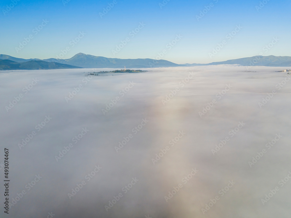 Flight over fog in Ukrainian Carpathians in summer. Mountains on the horizon. A thick layer of fog covers the mountains with a continuous carpet. Aerial drone view.