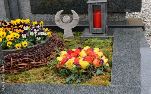 Obraz na płótnie Mit Blumen geschmückte Gräber an einem katholischen Friedhof in Österreich, ein Blumengebinde mit Rosen, daneben eine Blumenschale mit Stiefmütterchen und ein Engel und eine Friedhofslaterne w salonie